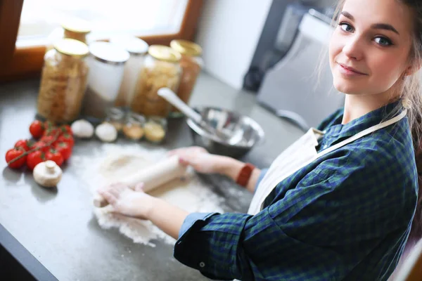 Güzel bir kadın mutfakta pasta pişiriyor. Masanın yanında duruyor..