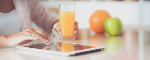 Mulher usando um computador tablet enquanto bebe suco em sua cozinha — Fotografia de Stock