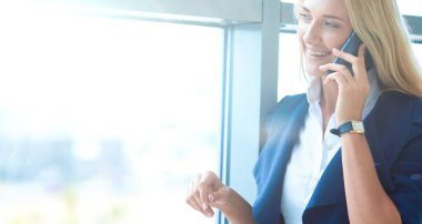 İş kadını ofis penceresinin önünde cep telefonuyla konuşuyor