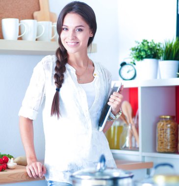 Mutfakta yemek yapmak için tablet bilgisayar kullanan genç bir kadın.