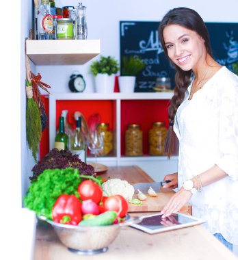 Mutfakta yemek yapmak için tablet bilgisayar kullanan genç bir kadın.