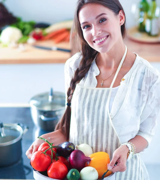 Souriante jeune femme tenant des légumes debout dans la cuisine — Photo