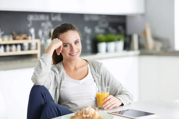 Ung kvinna med apelsinjuice och tablett i köket. — Stockfoto