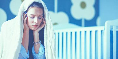 Yatakta çocuk karyolası yakın oturan genç yorgun kadın