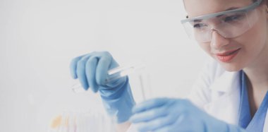 Kadın araştırmacı, beyaz arka planda izole edilmiş ilaç şişeleri ve mataralarla çevrili.