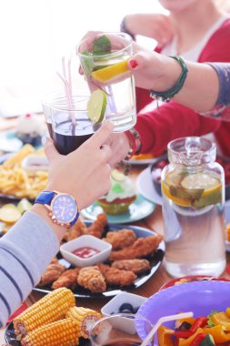 Ahşap masada otururken birlikte yemek yiyen bir grup insanın üst düzey görüntüsü. Masada yemek var. İnsanlar fast food yiyor..