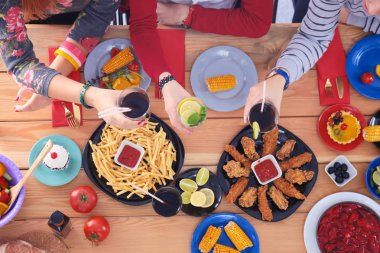 Ahşap masada otururken birlikte yemek yiyen bir grup insanın üst düzey görüntüsü. Masada yemek var. İnsanlar fast food yiyor..
