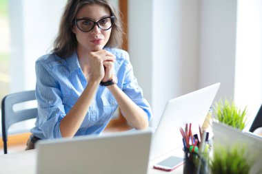 Ofis masasında dizüstü bilgisayarla oturan genç bir kadın. Genç bir kadın. Dizüstü bilgisayar