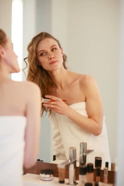 Genç bir kadın aynaya bakıyor ve makyaj yapıyor..