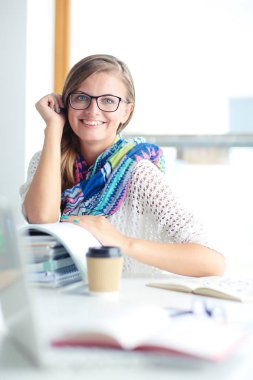 Kitapların arasında bir masada oturan genç bir kadın. Öğrenci