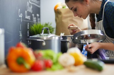 Mutfakta sobanın yanında duran genç bir kadın. .