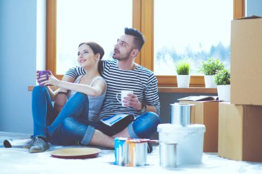 Yeni evin içini boyayan mutlu, gülümseyen genç bir çift portresi. Genç çift