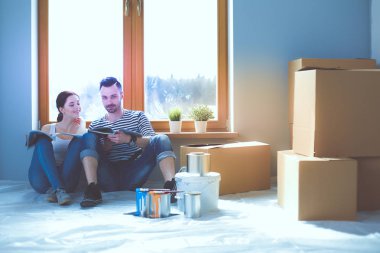 Yeni evin içini boyayan mutlu, gülümseyen genç bir çift portresi. Genç çift