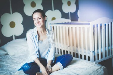 Yatakta çocuk karyolası yakın oturan bir genç bayan. Genç anne