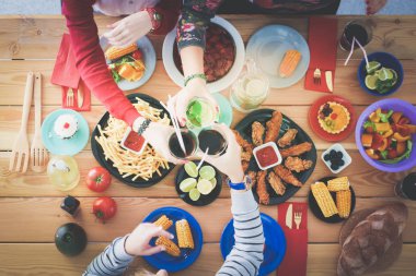 Ahşap masada otururken birlikte yemek yiyen bir grup insanın üst düzey görüntüsü. Masada yemek var. İnsanlar fast food yiyor..