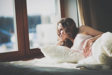 Pencere yakınındaki erken sabah yatakta yatan kadın.