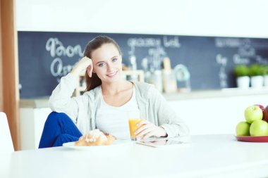 Mutfakta portakal suyu ve tableti olan genç bir kadın..