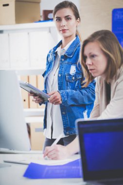 Masanın yanında duran iki genç kadın enstrüman, plan ve dizüstü bilgisayarla.