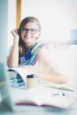 Kitapların arasında bir masada oturan genç bir kadın. Öğrenci