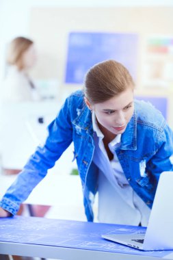 Masanın yanında duran iki genç kadın enstrüman, plan ve dizüstü bilgisayarla.