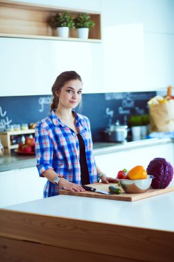 Masanın yanındaki mutfakta sebze doğrayan genç bir kadın..
