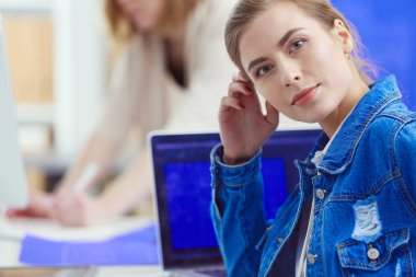 İki genç kadın masada enstrümanlar, planlar ve dizüstü bilgisayarlarla oturuyor..