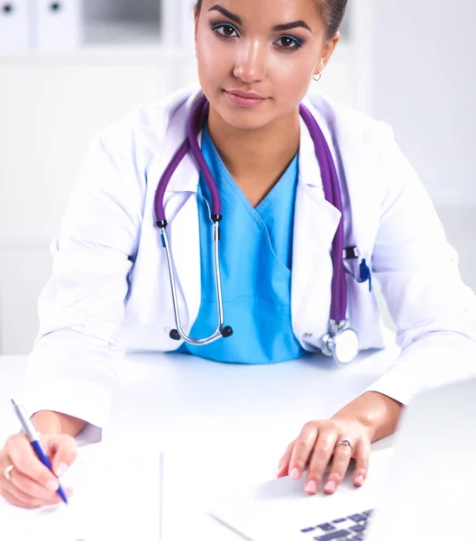 Hermosa joven sonriente doctora sentada en el escritorio y escribiendo. —  Fotos de Stock