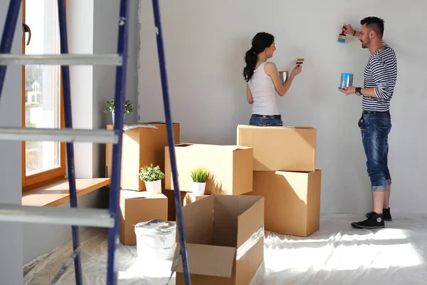 Portret van een vrolijk glimlachend jong stel dat de binnenmuur van een nieuw huis schildert. jong stel — Stockfoto