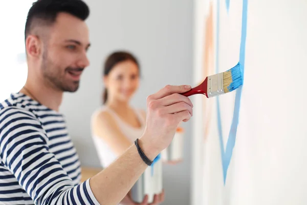 Portret van een vrolijk glimlachend jong stel dat de binnenmuur van een nieuw huis schildert. jong stel — Stockfoto