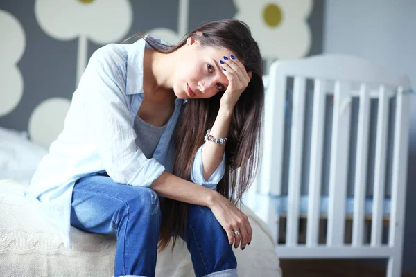 Genç çocuk karyolası yakın yatağın üstüne oturan kadın yorgun. Genç anne.