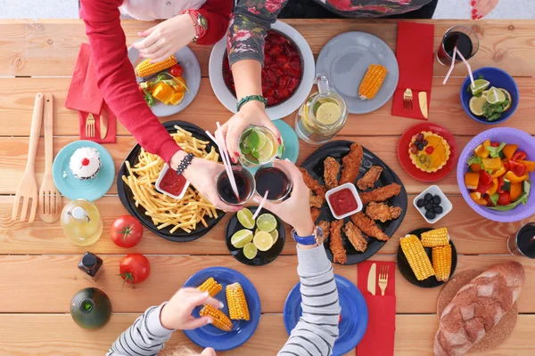 Ahşap masada otururken birlikte yemek yiyen bir grup insanın üst düzey görüntüsü. Masada yemek var. İnsanlar fast food yiyor..