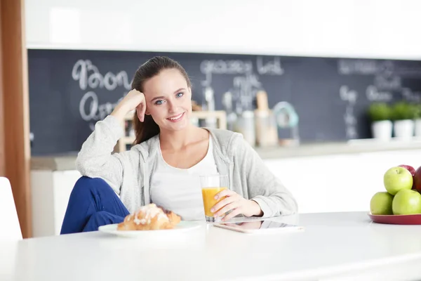 Młoda kobieta z sokiem pomarańczowym i tabletką w kuchni. — Zdjęcie stockowe