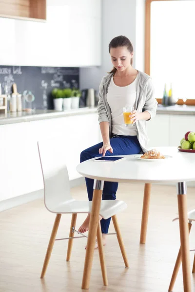 Ung kvinna med apelsinjuice och tablett i köket. — Stockfoto
