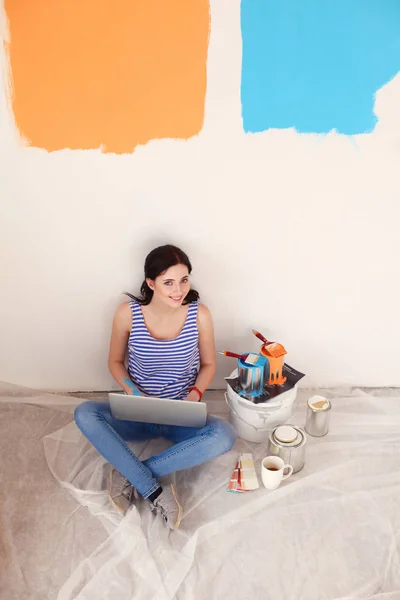 Portret van de jonge vrouw tijdens het schilderen van nieuw appartement, zitten met laptop. Jonge vrouw met laptop — Stockfoto