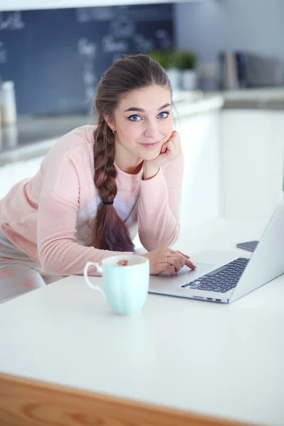 Junge Frau sitzt mit Laptop am Küchentisch und telefoniert. — Stockfoto