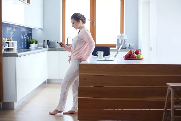 Mujer usando el teléfono móvil de pie en la cocina moderna . — Foto de Stock