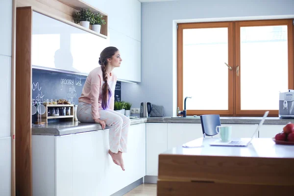 Молодая женщина сидит на столе на кухне . — стоковое фото