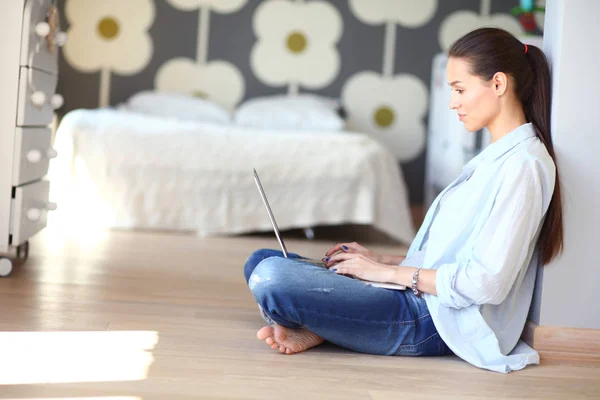 Jonge vrouw zittend op de vloer in de buurt van childrens kinderbed met laptop. Jonge moeder — Stockfoto