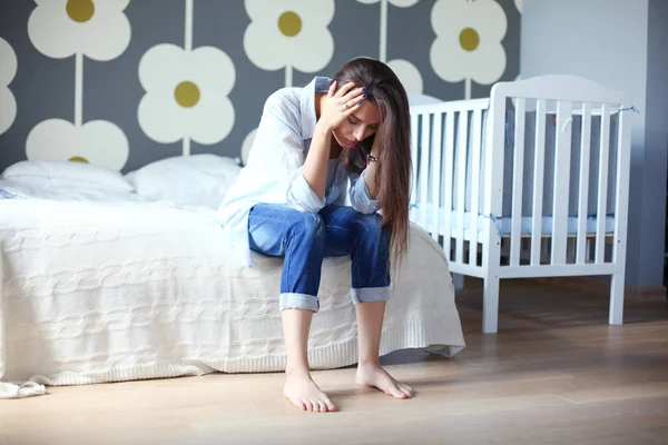 Ung trött kvinna som sitter på sängen nära barnens spjälsäng. Ung mamma. — Stockfoto