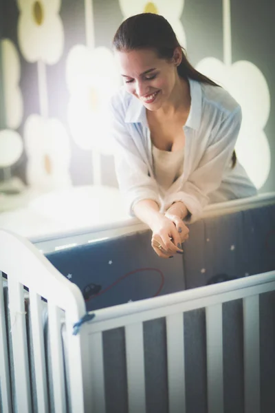 Jonge vrouw stond in de buurt van childrens kinderbed. Jonge moeder — Stockfoto