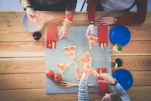 Ahşap masada otururken birlikte yemek yiyen bir grup insanın üst düzey görüntüsü. Masada yemek var. İnsanlar fast food yiyor..