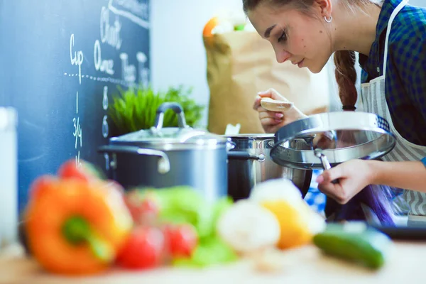 Mujer joven parada junto a la estufa en la cocina . — Foto de Stock