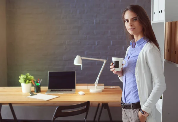 Retrato de una joven relajada sentada en su escritorio sosteniendo una taza de café. Mujer de negocios. Lugar de trabajo. — Foto de Stock