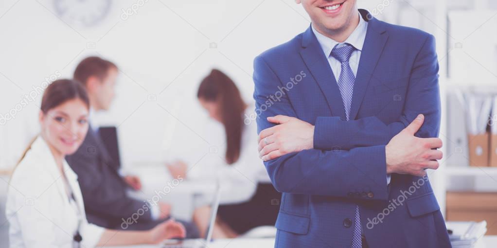 Successful business man standing with his staff in background at office