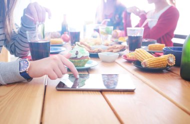 Ahşap masada otururken birlikte yemek yiyen bir grup insanın üst düzey görüntüsü. Masada yemek var. İnsanlar fast food yiyor..