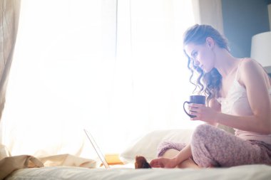 Dizüstü bilgisayar ile yatakta oturan genç güzel kadın.