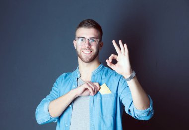 Gri arka planda duran bir kredi kartı tutan genç adam. Genç girişimci..