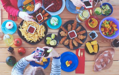 Ahşap masada otururken birlikte yemek yiyen bir grup insanın üst düzey görüntüsü. Masada yemek var. İnsanlar fast food yiyor..