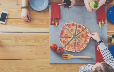 Ahşap masada otururken birlikte yemek yiyen bir grup insanın üst düzey görüntüsü. Masada yemek var. İnsanlar fast food yiyor..
