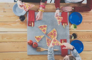 Ahşap masada otururken birlikte yemek yiyen bir grup insanın üst düzey görüntüsü. Masada yemek var. İnsanlar fast food yiyor..
